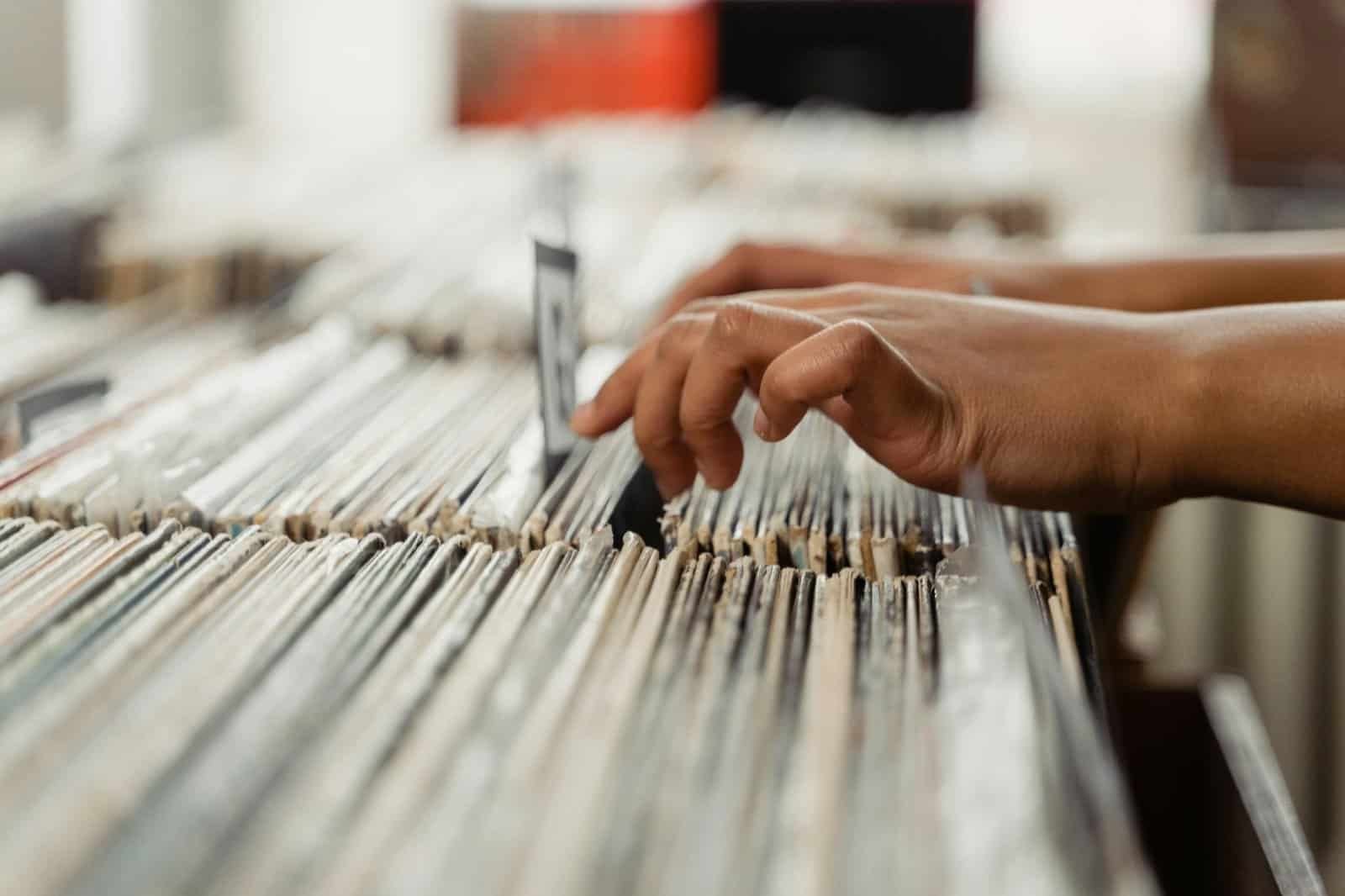 Vintage vinyl record collection being played with a person's hand browsing through the records, emphasizing the love for classic music, vinyl records, and turntable culture at VibeTheVINYL.