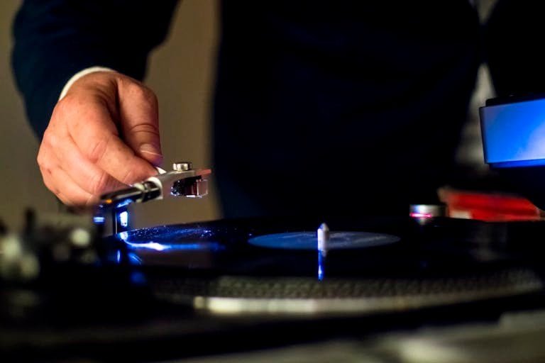 Close-up of hand adjusting a needle on a vintage turntable, playing a vinyl record indoors.