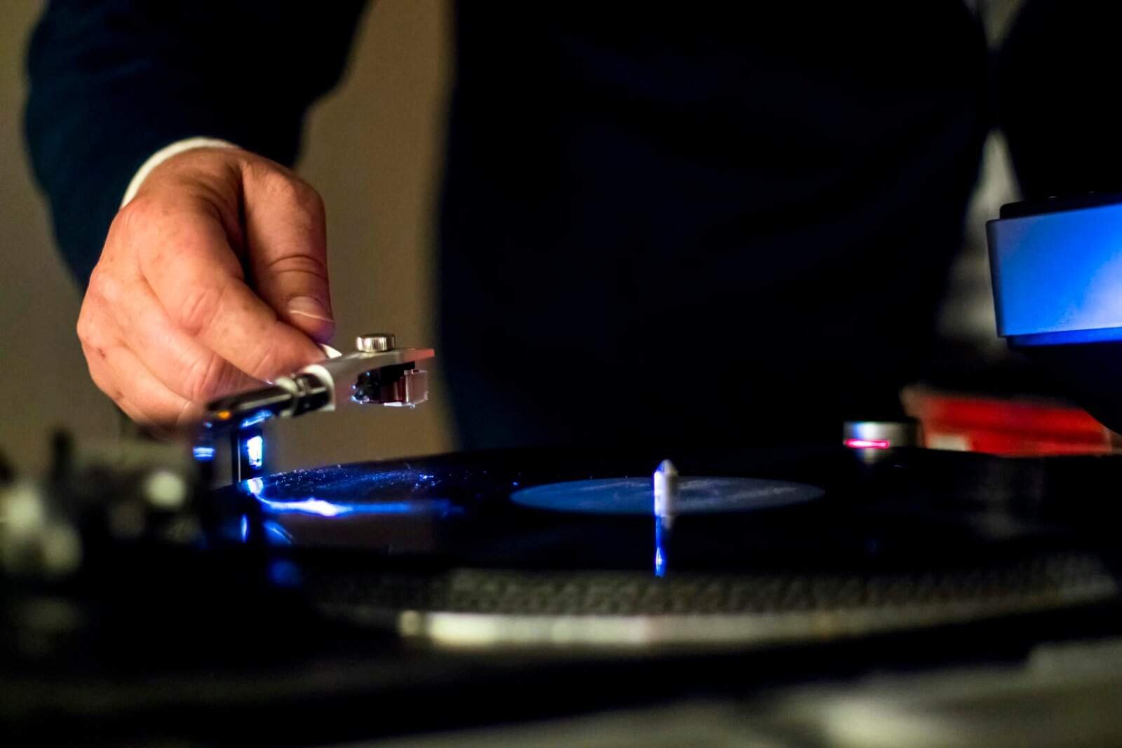 Close-up of hand adjusting a needle on a vintage turntable, playing a vinyl record indoors.